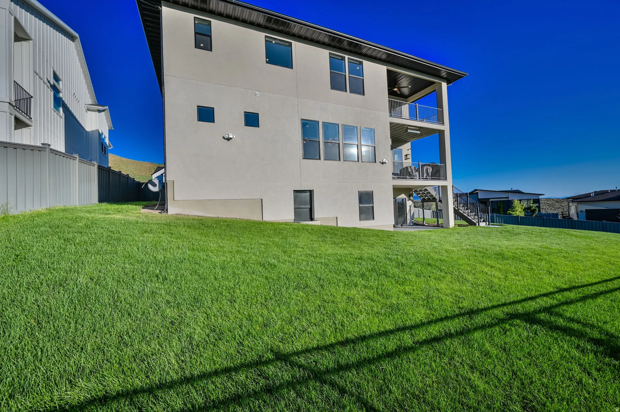 Expansive green lawn with a multi-level concrete exterior home featuring two covered balconies with glass railings