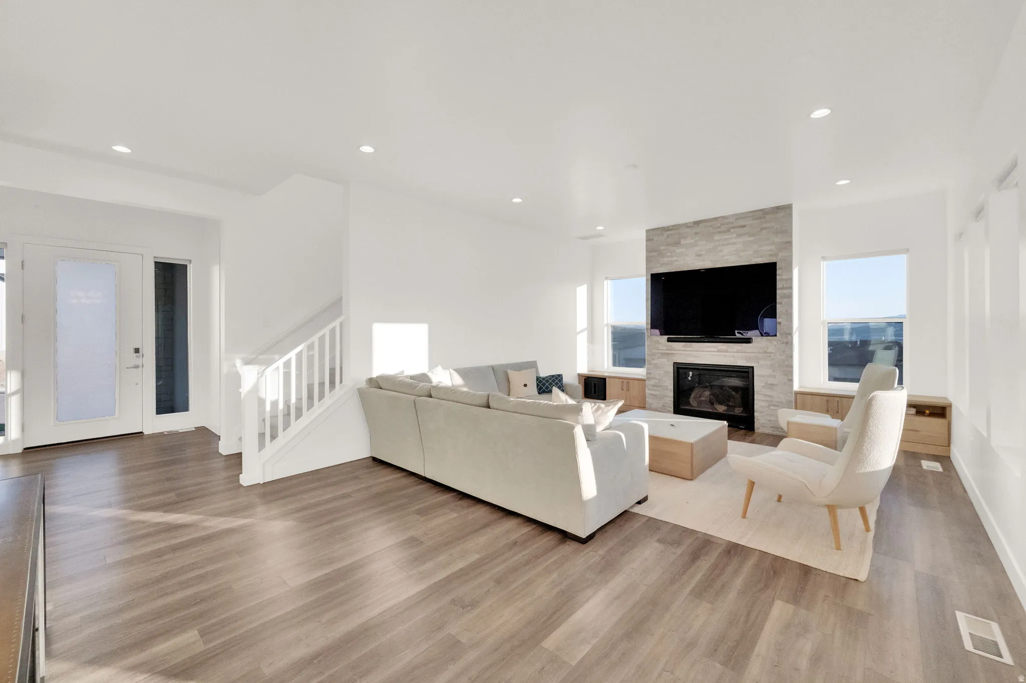 Open-concept living area featuring wood-finish flooring, a contemporary fireplace with a stacked stone facade, recessed lighting, and large windows