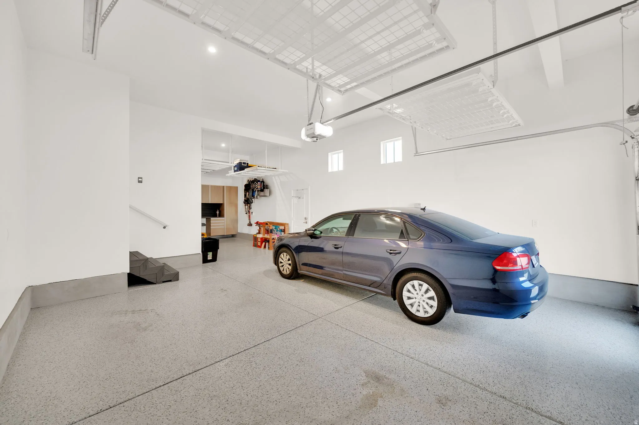 Spacious garage featuring epoxy flooring, built-in cabinetry, overhead storage racks, and multiple windows