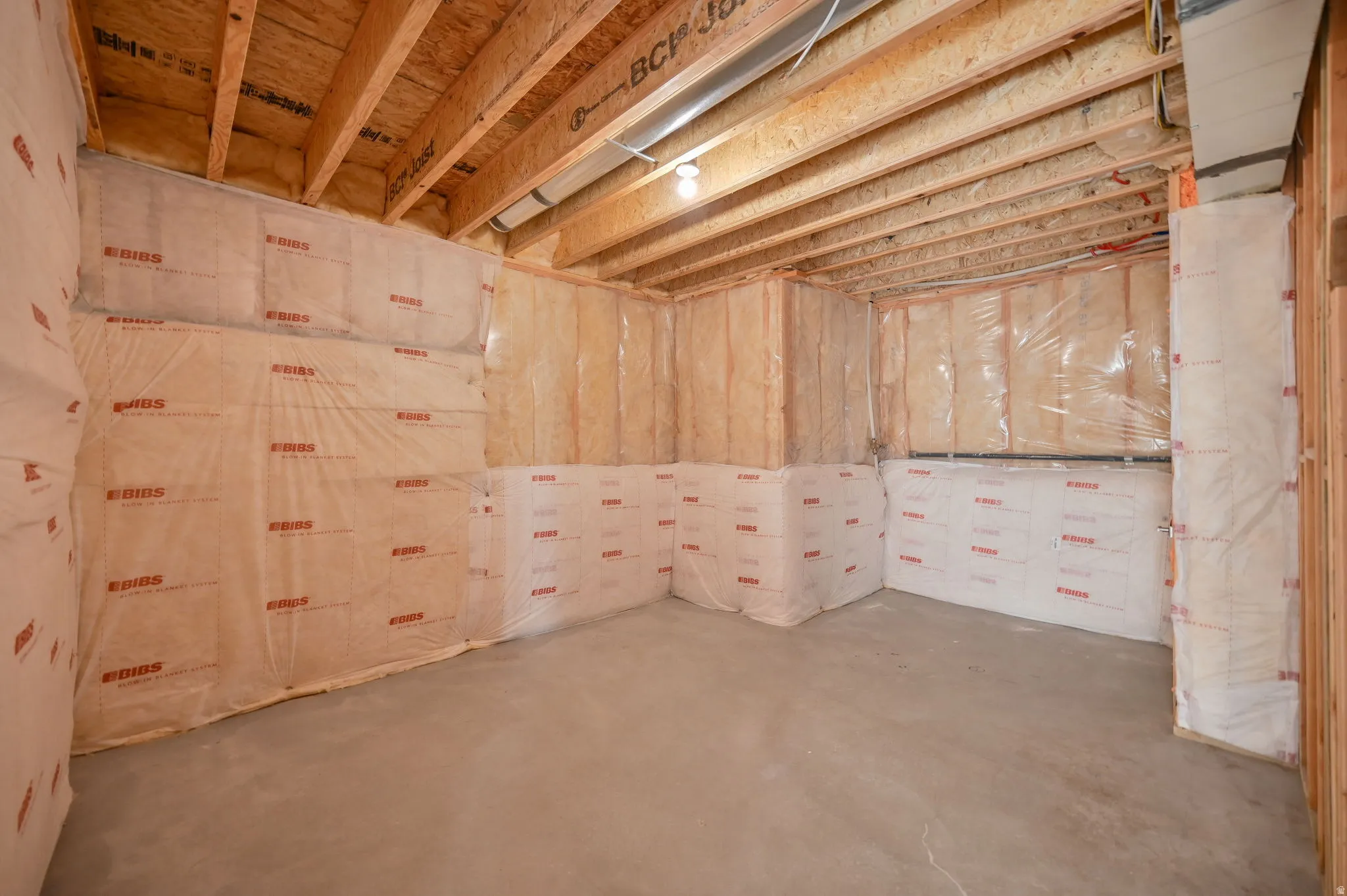 Unfinished lower level featuring exposed wood joists, insulated walls, and a concrete floor