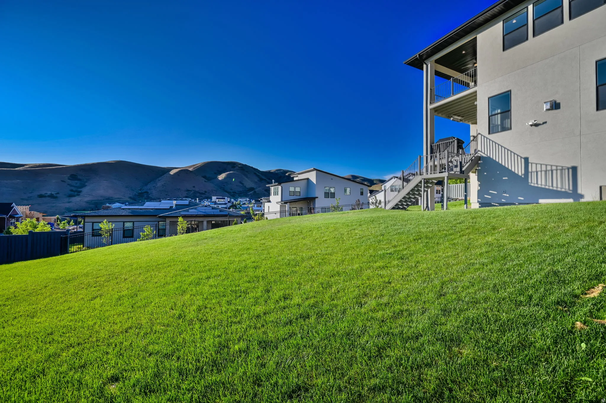 Expansive green lawn with a two-story residence featuring a ground-level patio, an upper-level balcony, and exterior stairs