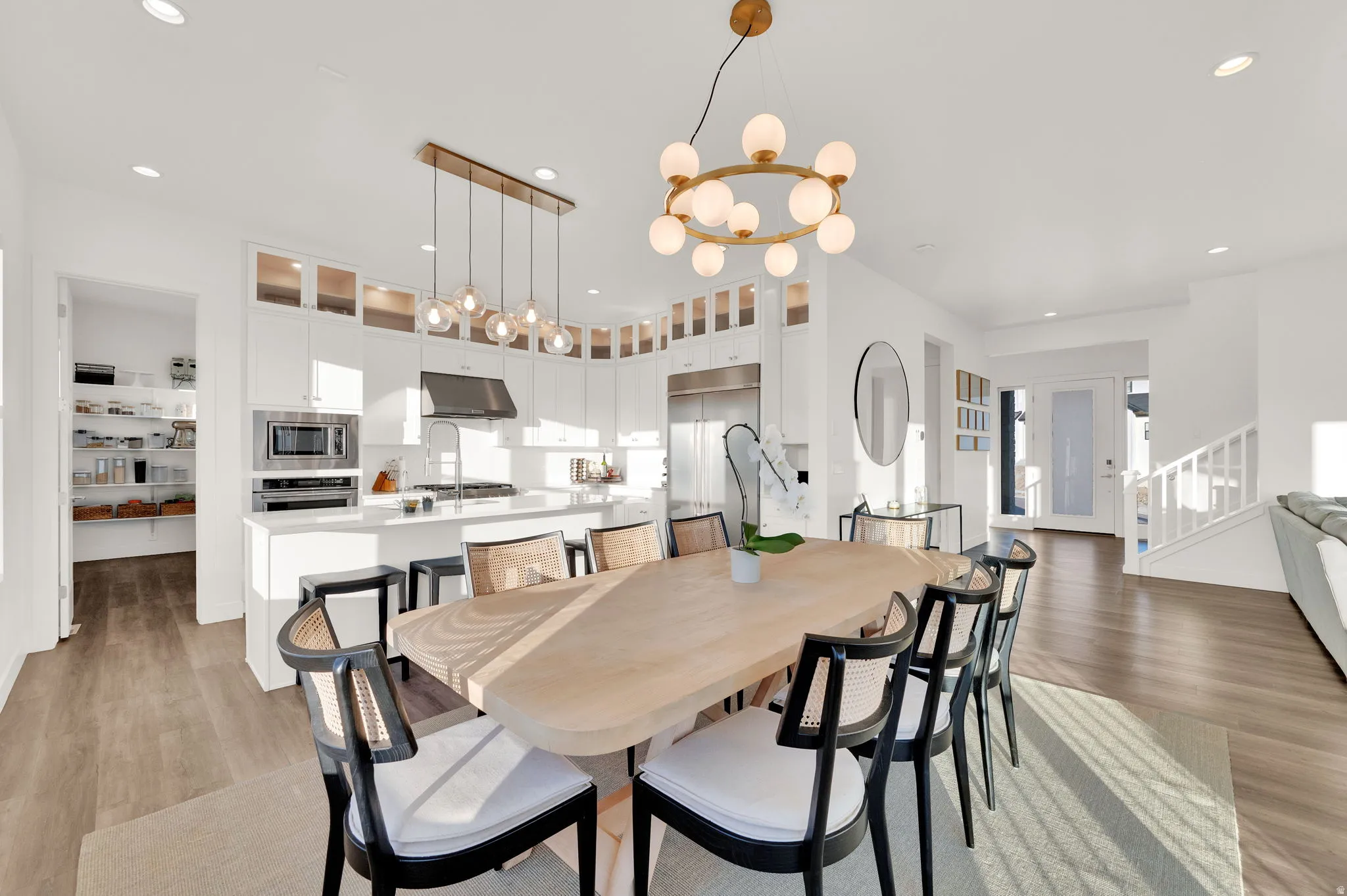 Open-concept living space featuring a dining area with a contemporary chandelier, wood-finish flooring, and a kitchen with white cabinetry, stainless steel appliances, and a walk-in pantry