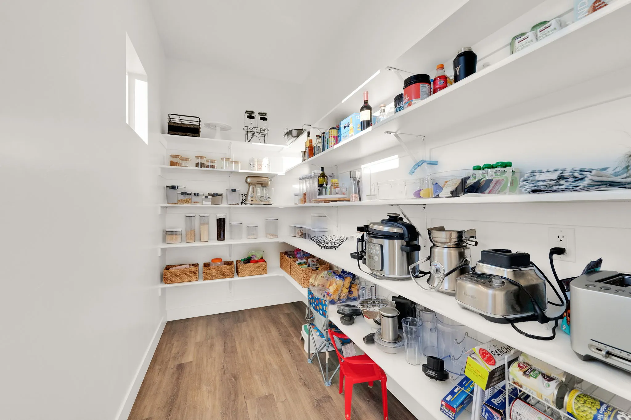 Walk-in pantry featuring extensive white shelving, wood-finish flooring, and natural light from a high window