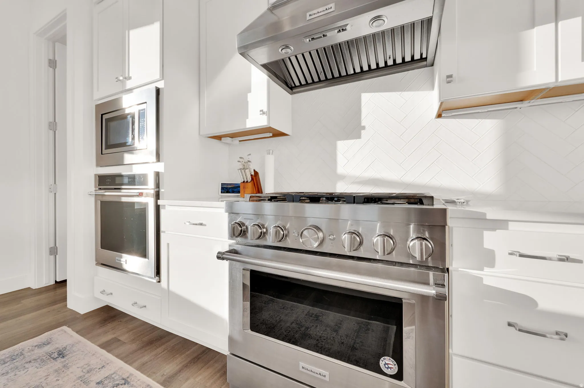 Stainless steel range with a professional-grade hood, surrounded by white cabinetry and a white herringbone tile backsplash