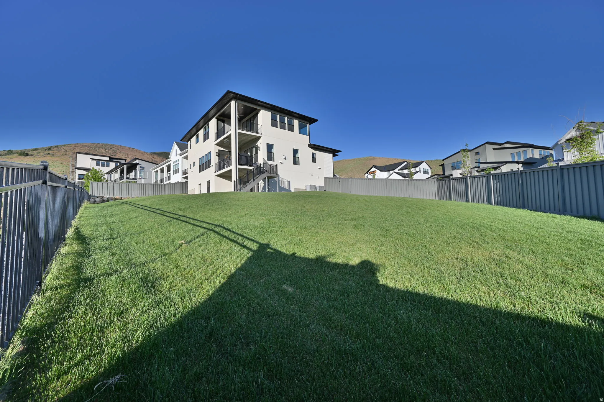 Expansive grassy yard area with a multi-level dwelling featuring three balconies with dark railings and a dark roofline