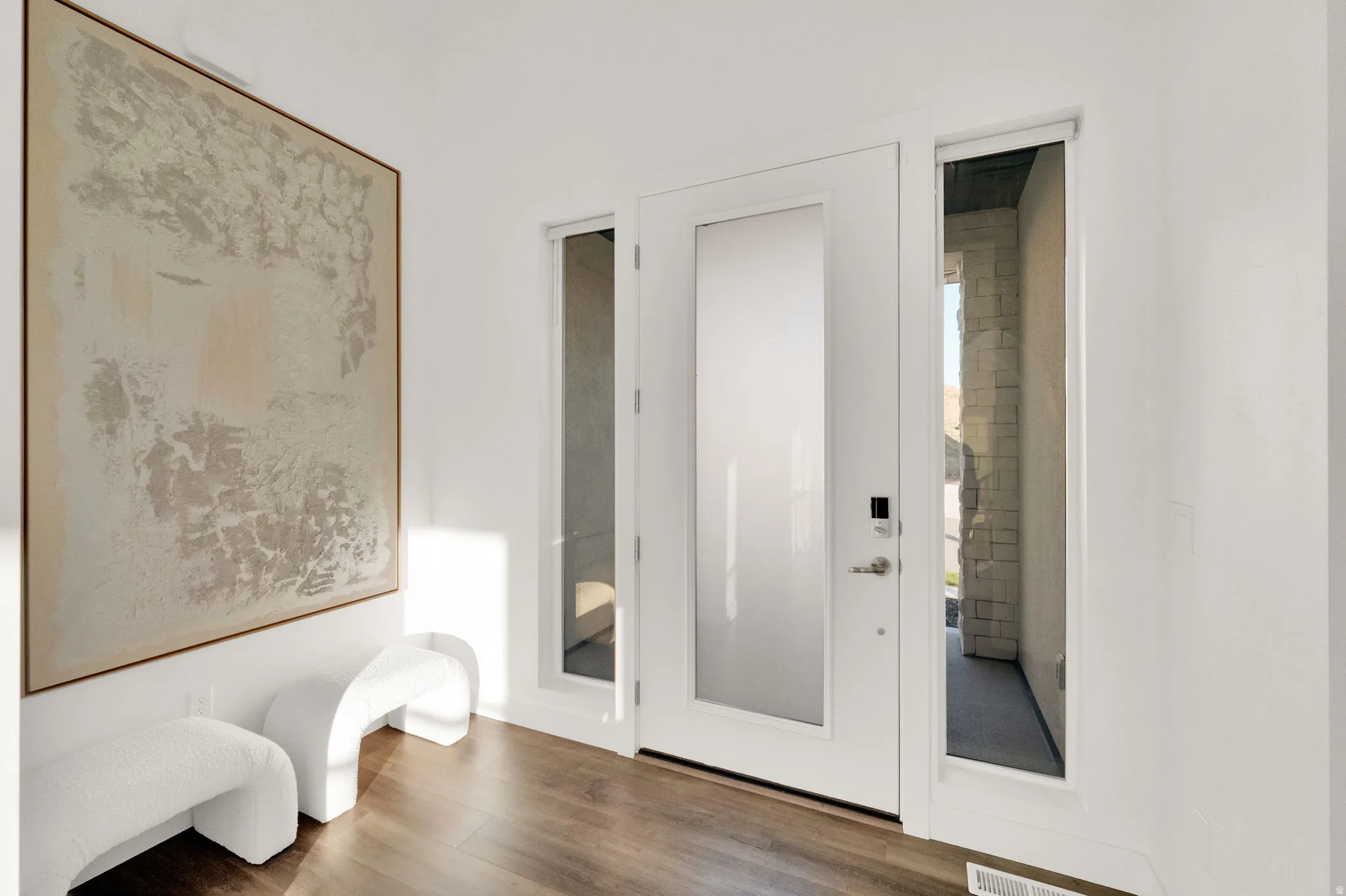 Modern entry door with frosted glass panel and adjacent sidelights, complemented by wood-finish flooring and bright white walls