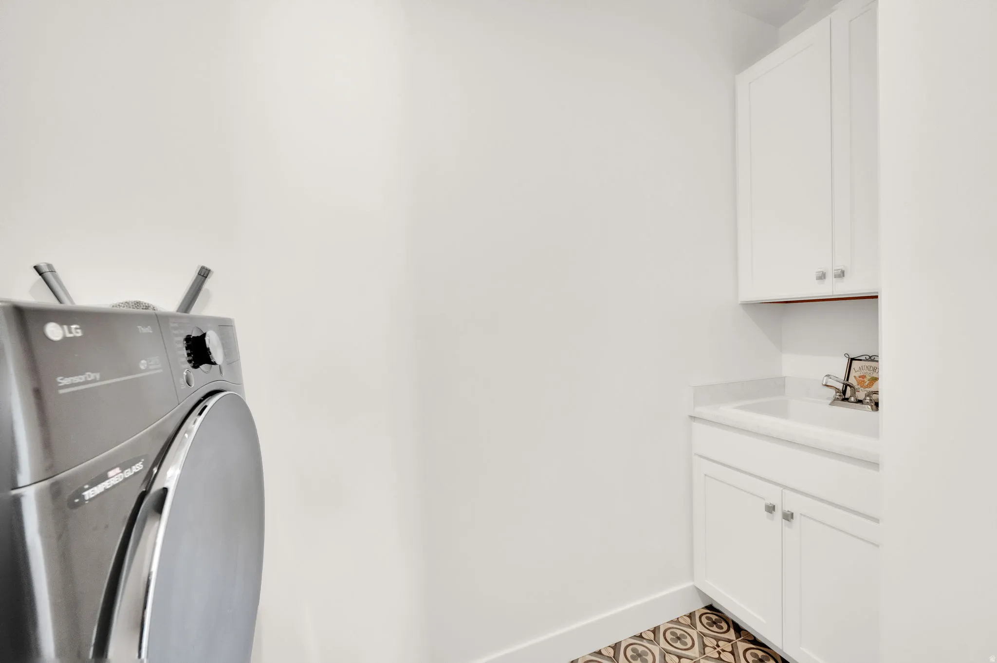 Dedicated utility area featuring white cabinetry, a built-in sink with a countertop, decorative floor tiling, and a front-loading appliance