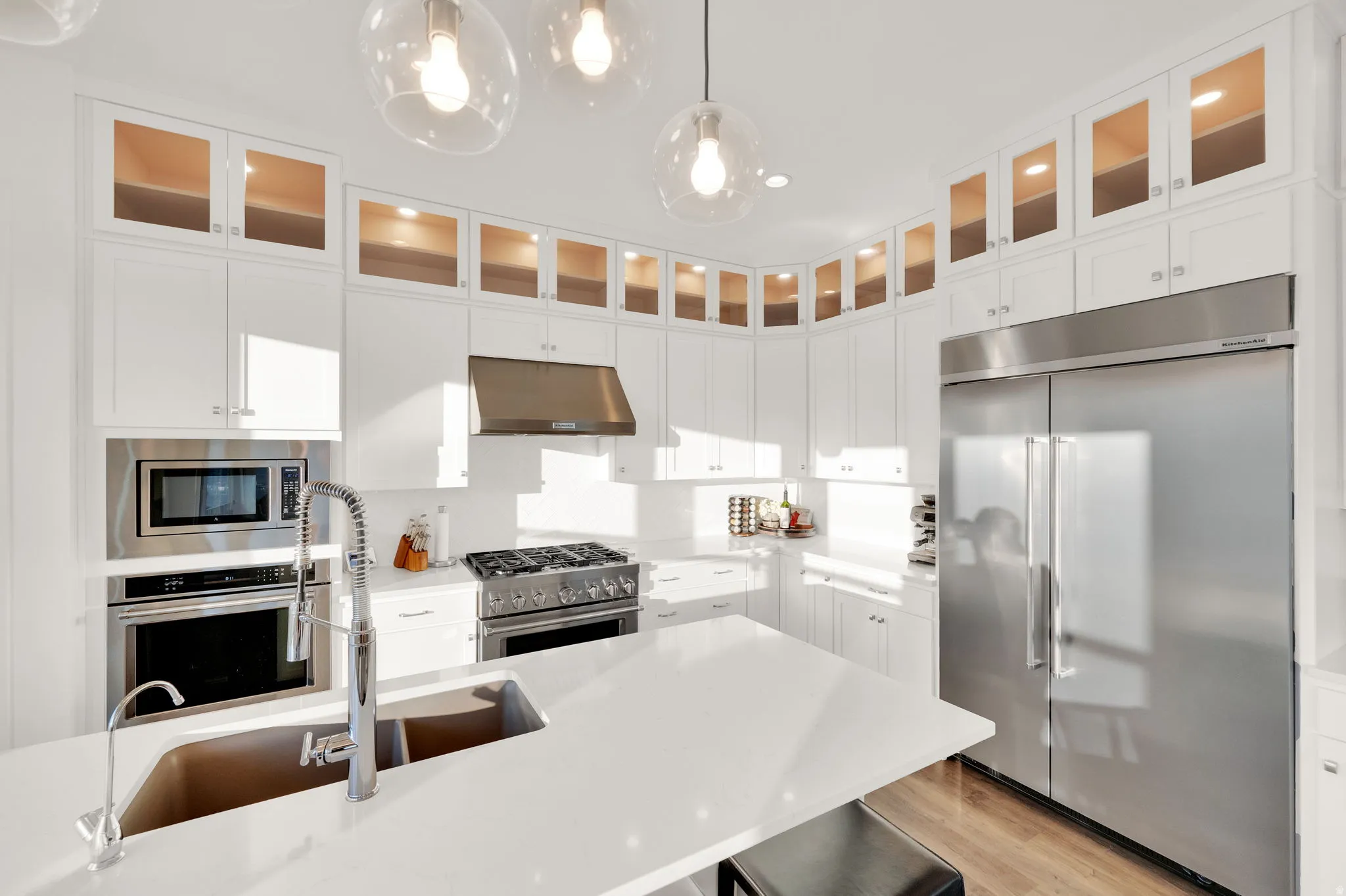 Gourmet kitchen featuring white cabinetry with glass-front upper cabinets, stainless steel appliances, a gas range with a coordinating hood, and a large center island with an integrated sink
