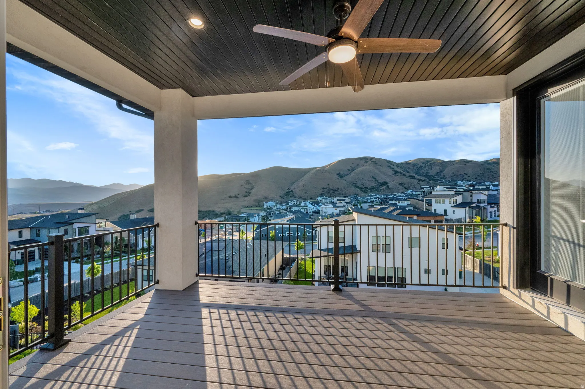 Covered outdoor deck featuring composite decking, black metal railings, a ceiling fan with integrated lighting, and mountain scenery