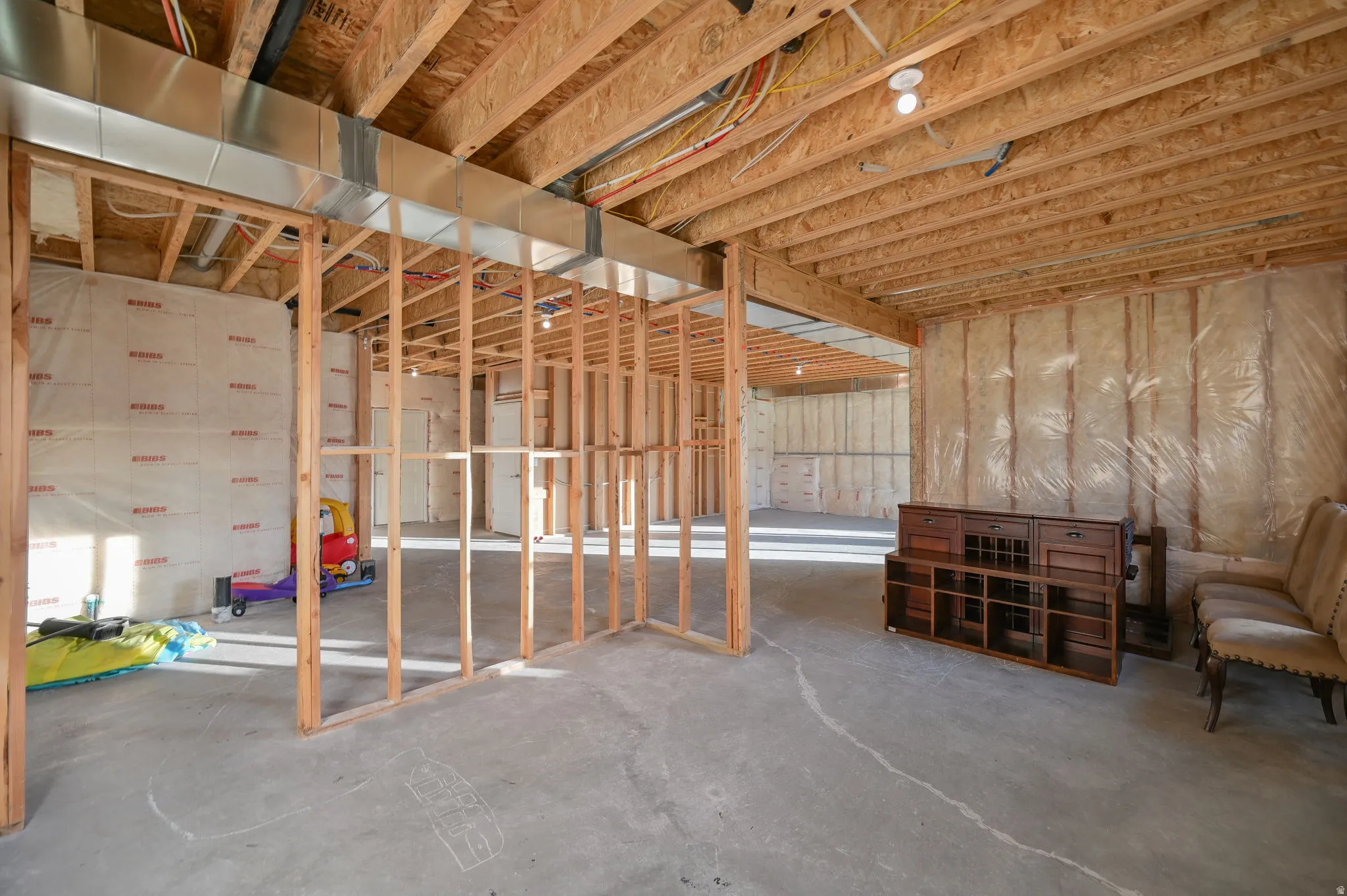 Unfinished basement featuring exposed wood framing, concrete flooring, insulated walls, and visible ductwork