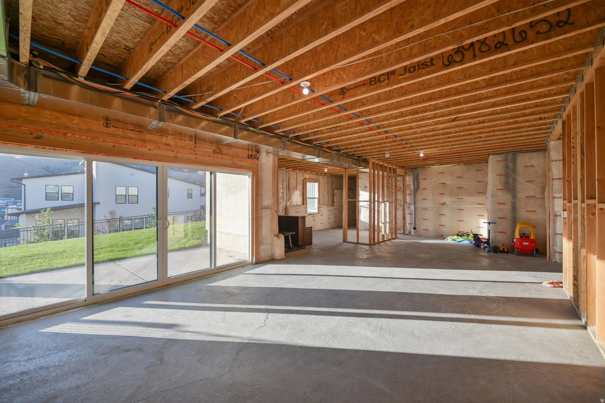 Unfinished interior space featuring exposed wood joists and framing, concrete flooring, and a large sliding glass door