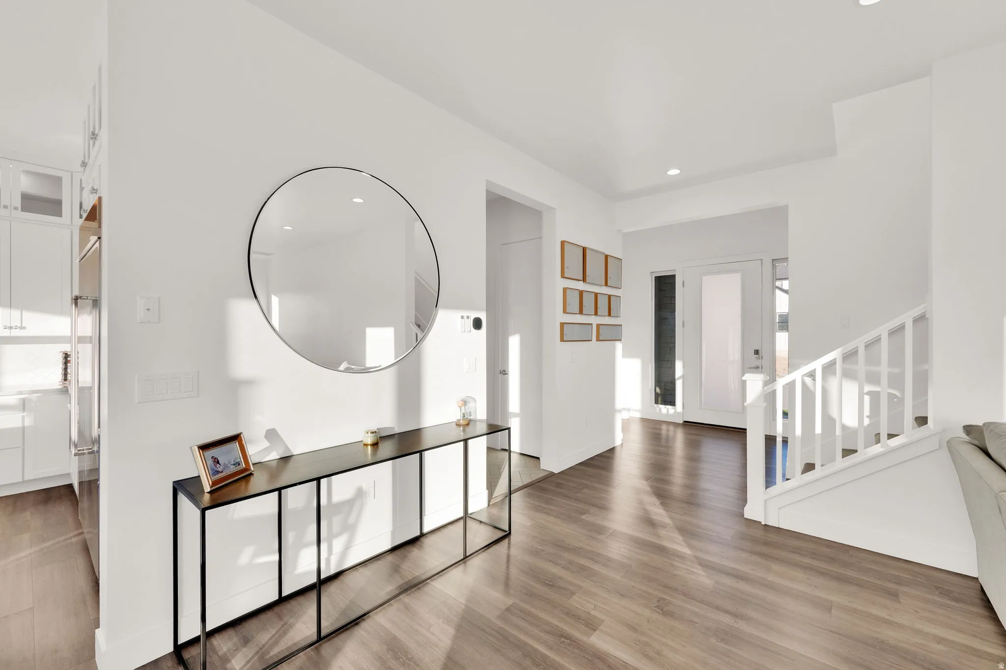 Bright entryway featuring wood-finish flooring, white walls, a staircase with white balusters, and a contemporary front door with frosted glass panels