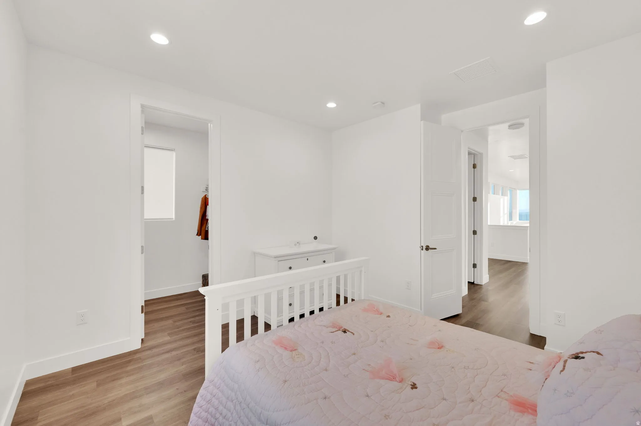 Bright interior space featuring recessed lighting, wood-finish flooring, white baseboards, and a white interior door with bronze hardware