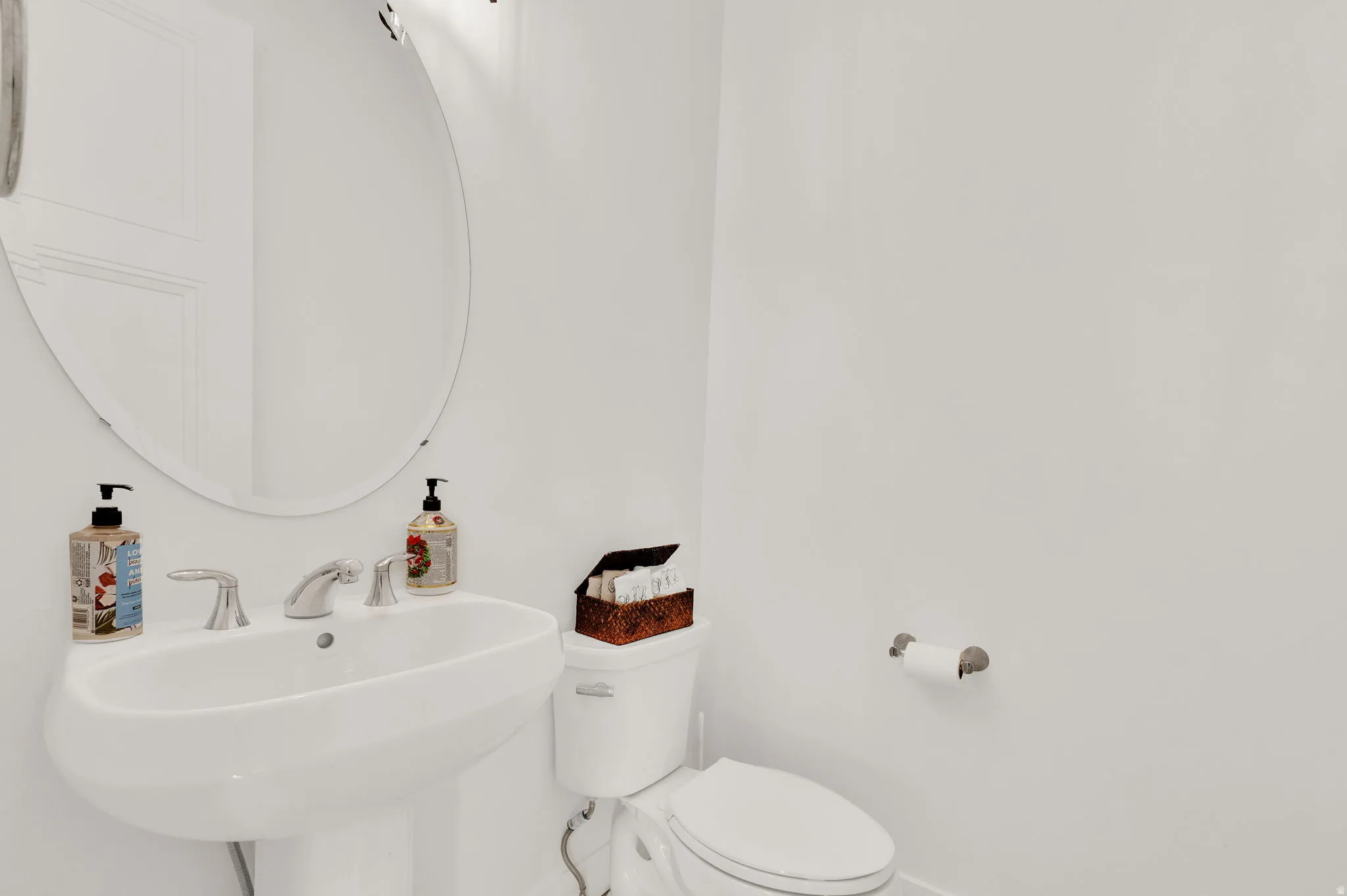 White pedestal sink with chrome fixtures and an oval wall-mounted mirror