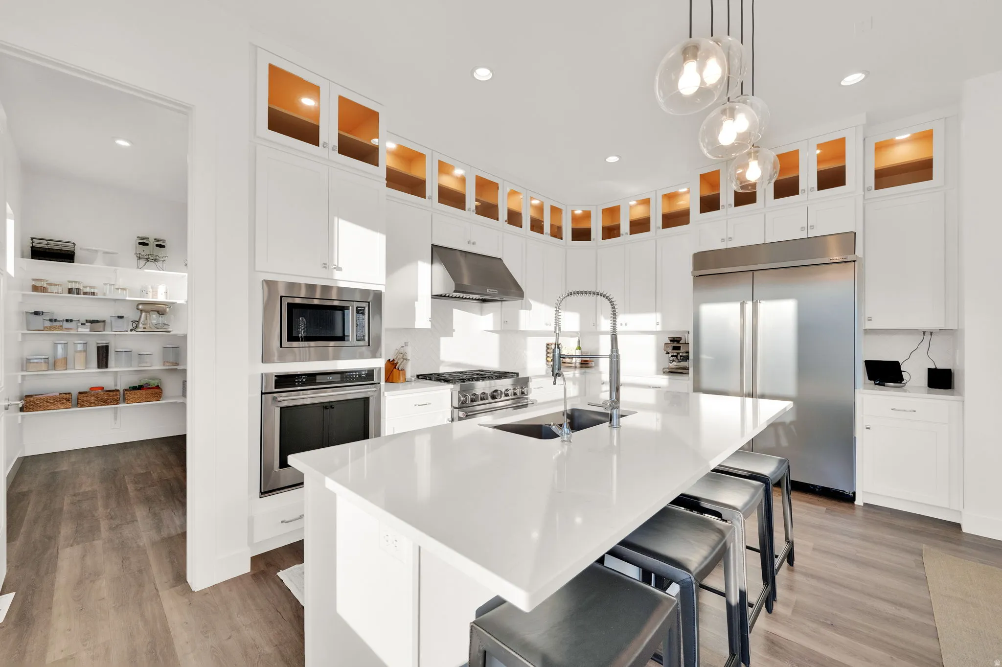 Gourmet kitchen featuring a large central island with seating, stainless steel appliances, white cabinetry with upper glass-front accents, and wood-finish flooring