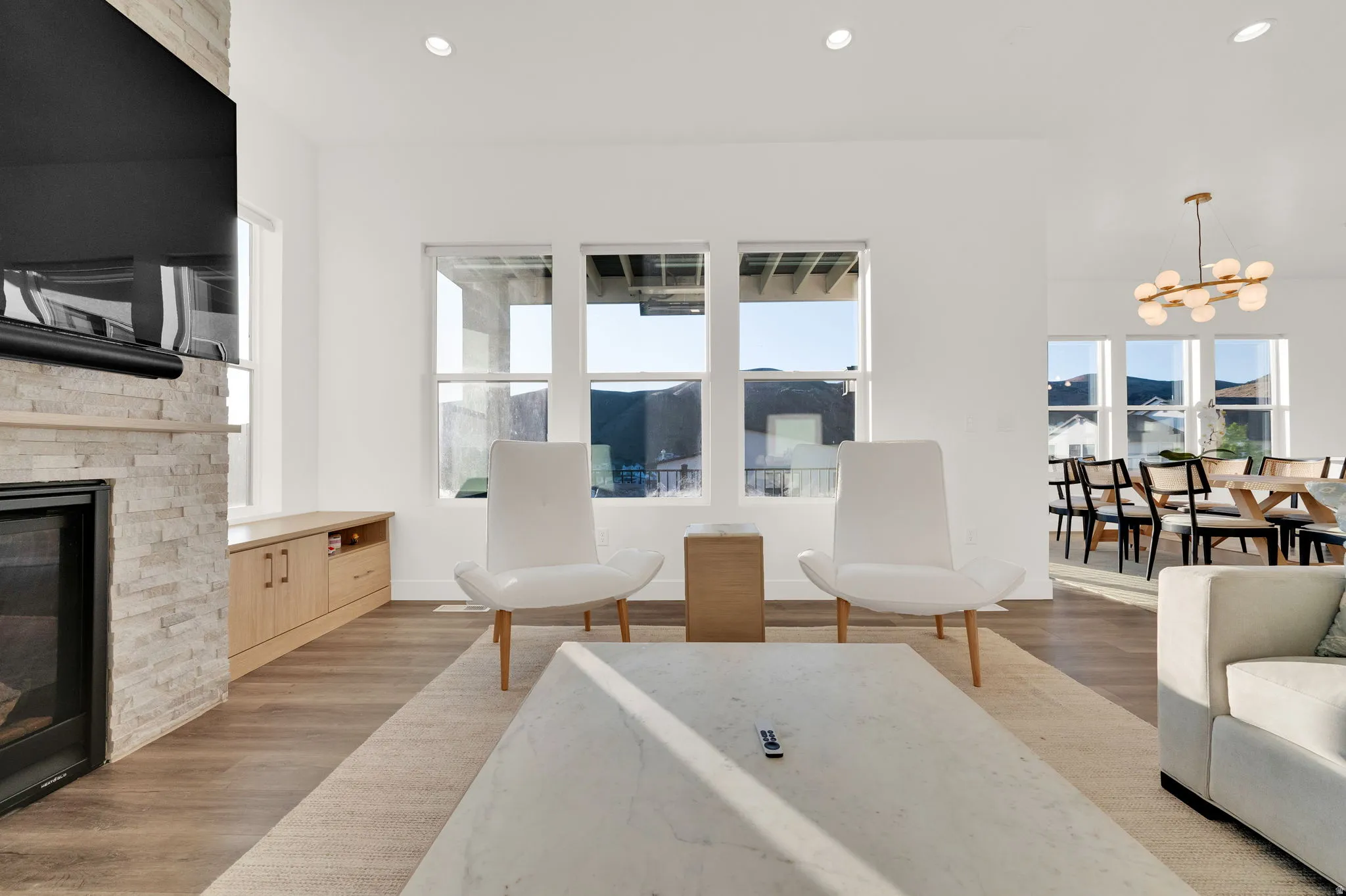 Open-concept living area with wood-finish flooring, a stone fireplace, recessed lighting, and multiple windows