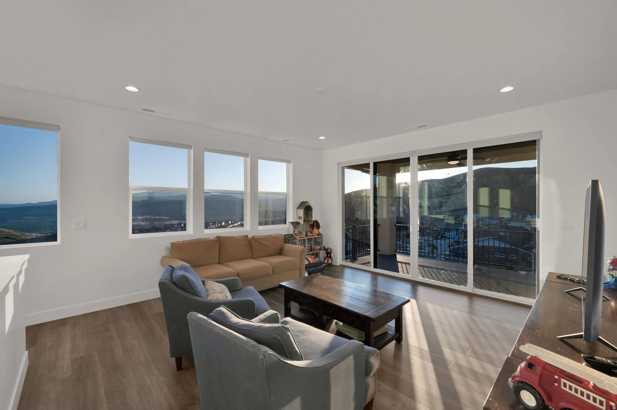 Light-filled living area featuring wood-finish flooring, a wall of windows, recessed lighting, white baseboards, and a glass sliding door opening to a balcony