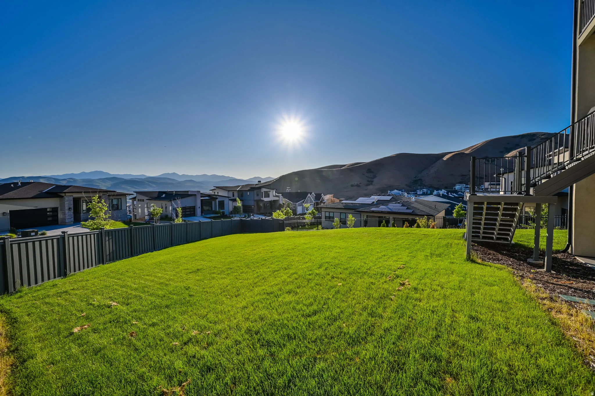 Expansive green lawn with a dark metal fence perimeter, offering a backdrop of distant mountains