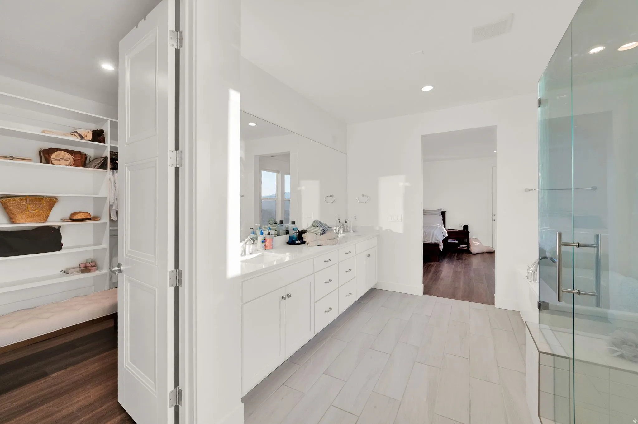 Bright bathroom featuring a double vanity with stone countertop, glass-enclosed shower, and wood-finish flooring