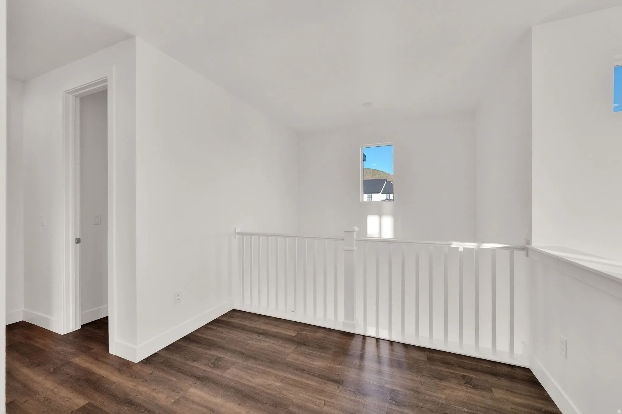 Open interior space featuring wood-finish flooring, white walls, and a white spindle railing