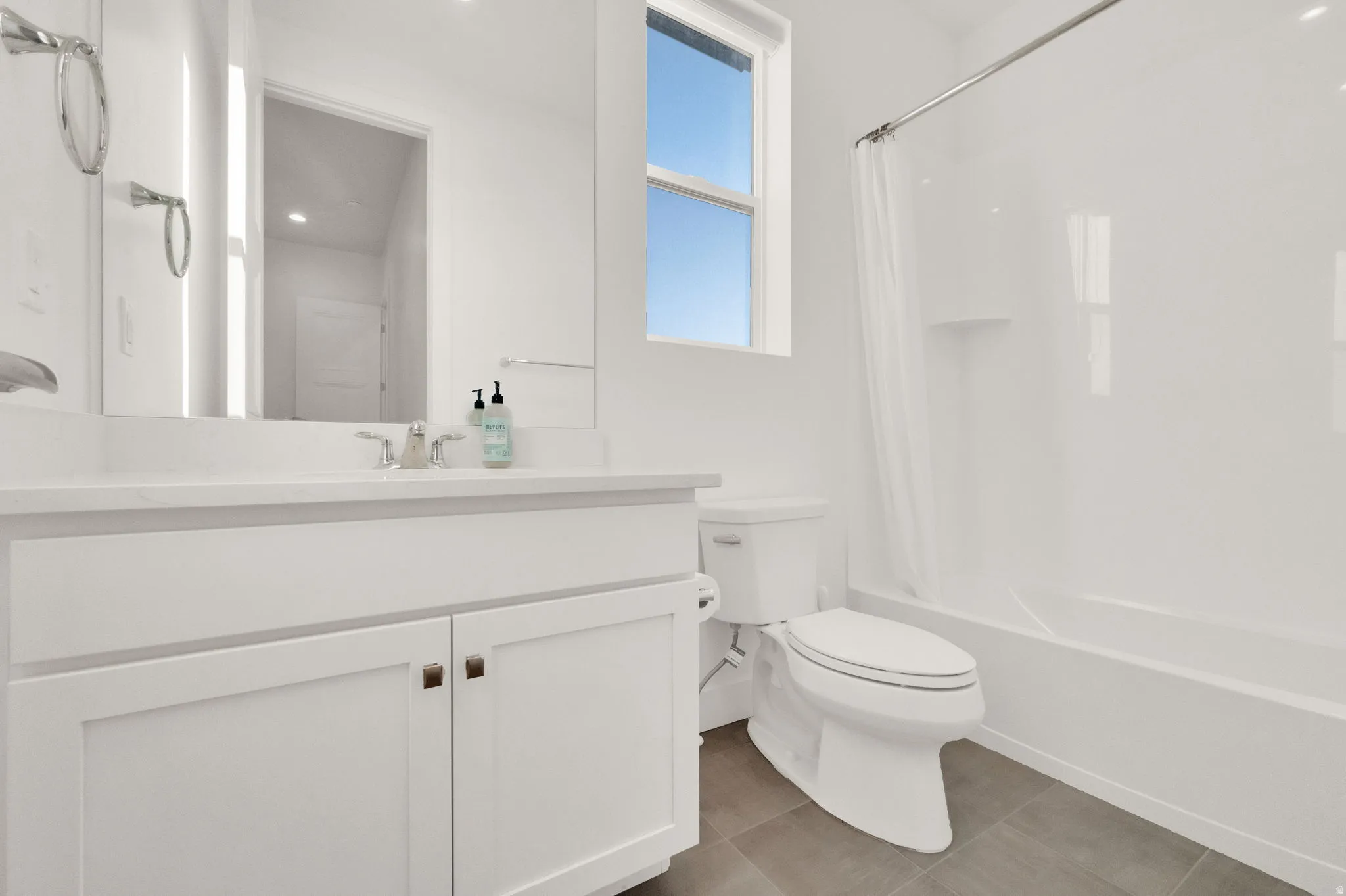 Contemporary bathroom featuring a white vanity with integrated sink, a built-in bathtub with shower, a window, and gray tiled flooring