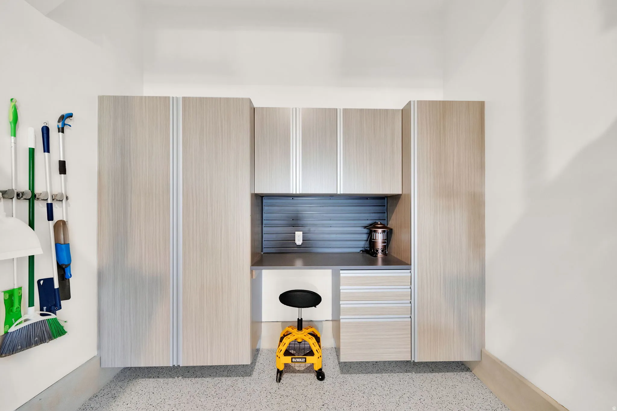 Integrated garage storage system featuring wood-finish cabinetry, a dedicated workstation with a gray countertop, and slatwall organization