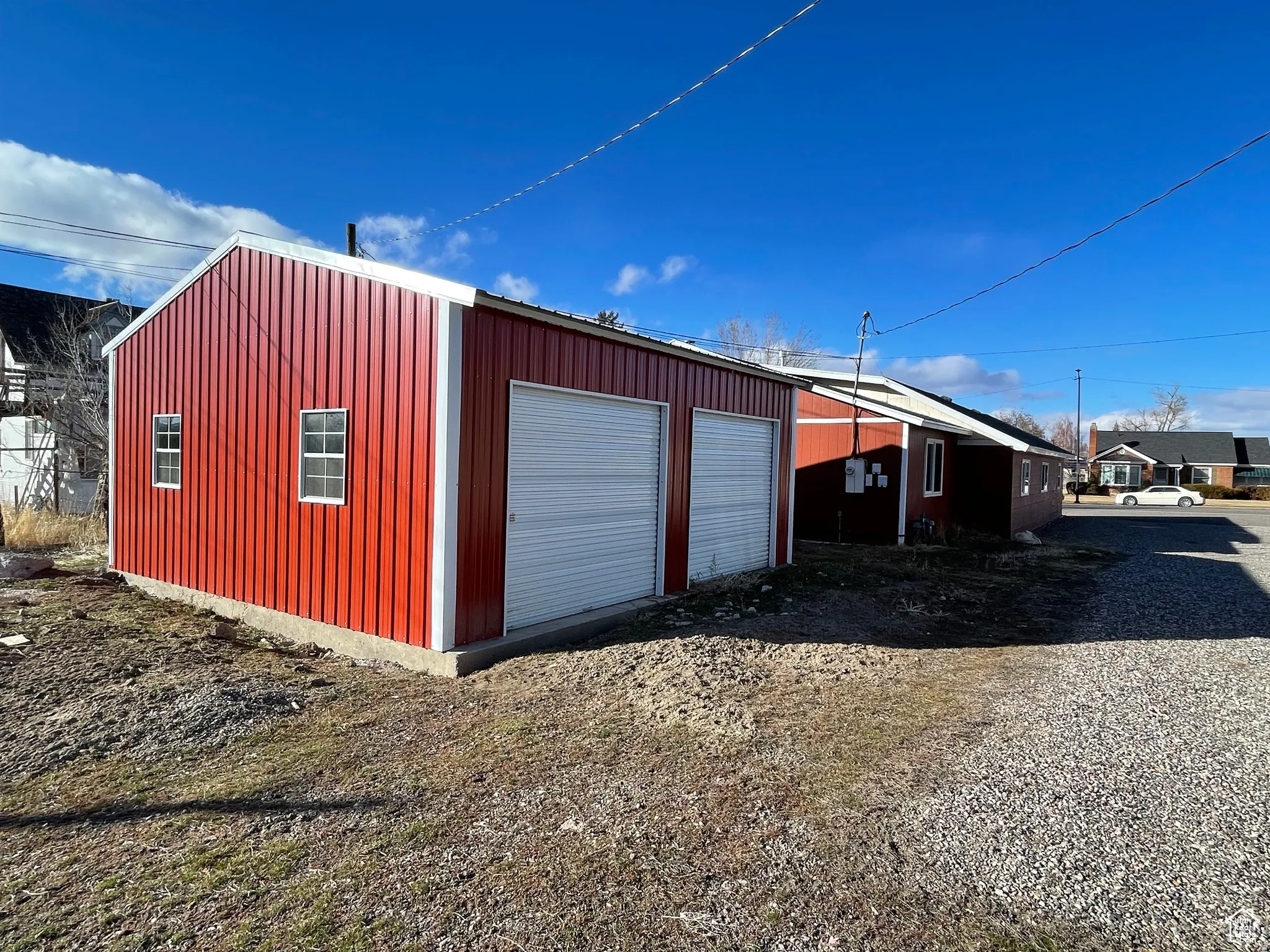 Red metal-sided outbuilding featuring a pitched roofline and two white roll-up garage doors