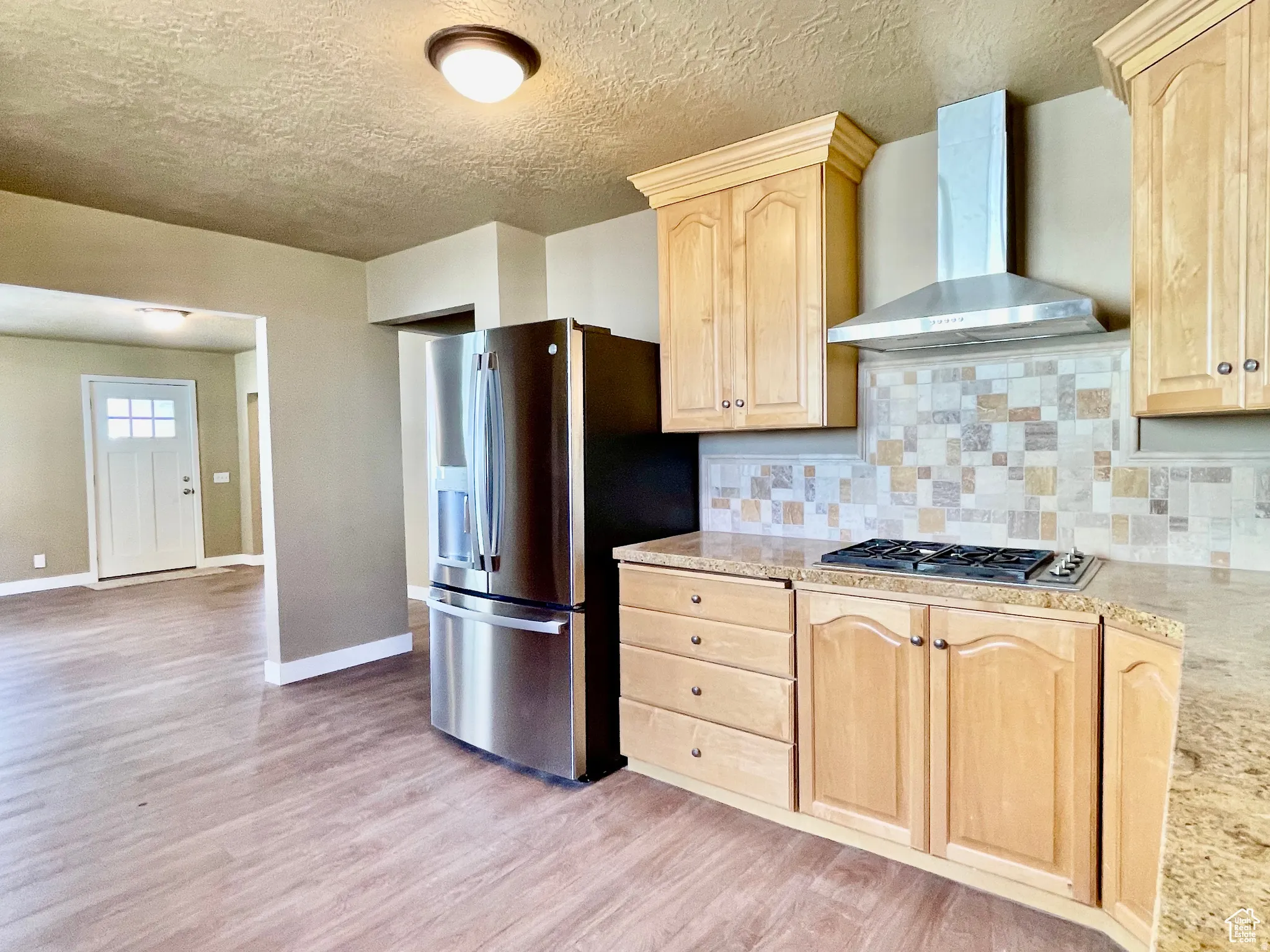 Kitchen featuring light wood-finish cabinetry, granite-style countertops, stainless steel appliances, and a mosaic tile backsplash