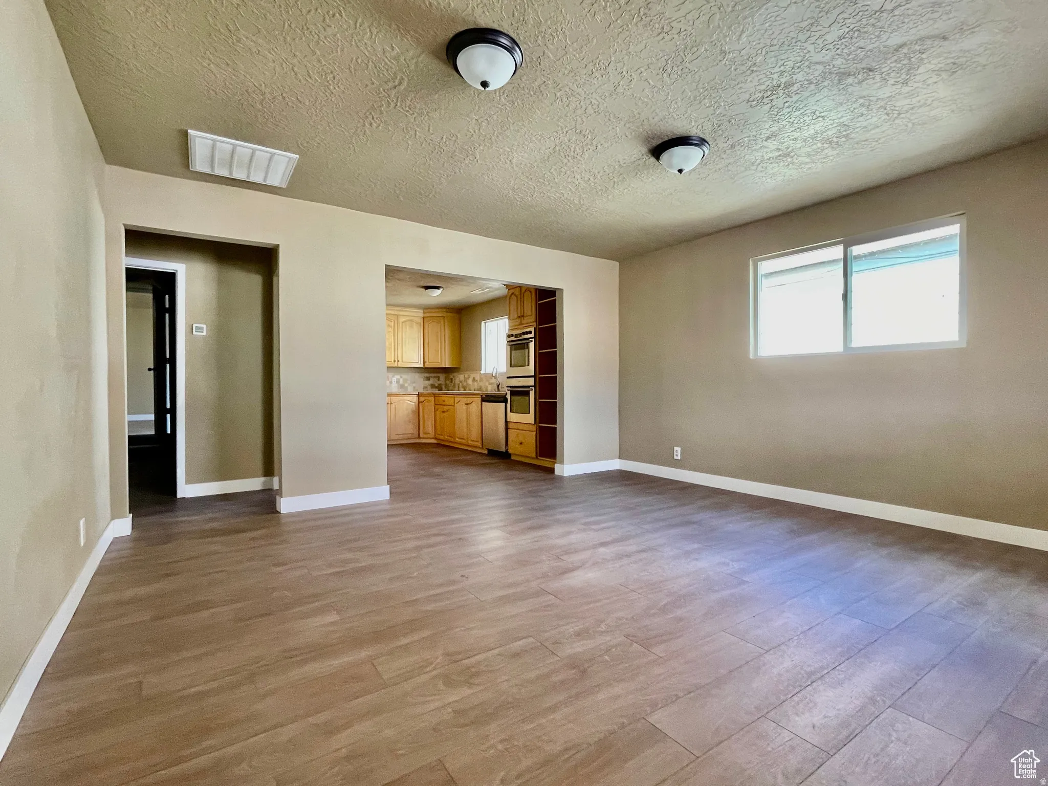Spacious room featuring wood-finish flooring, neutral-toned walls, and abundant natural light from a large window