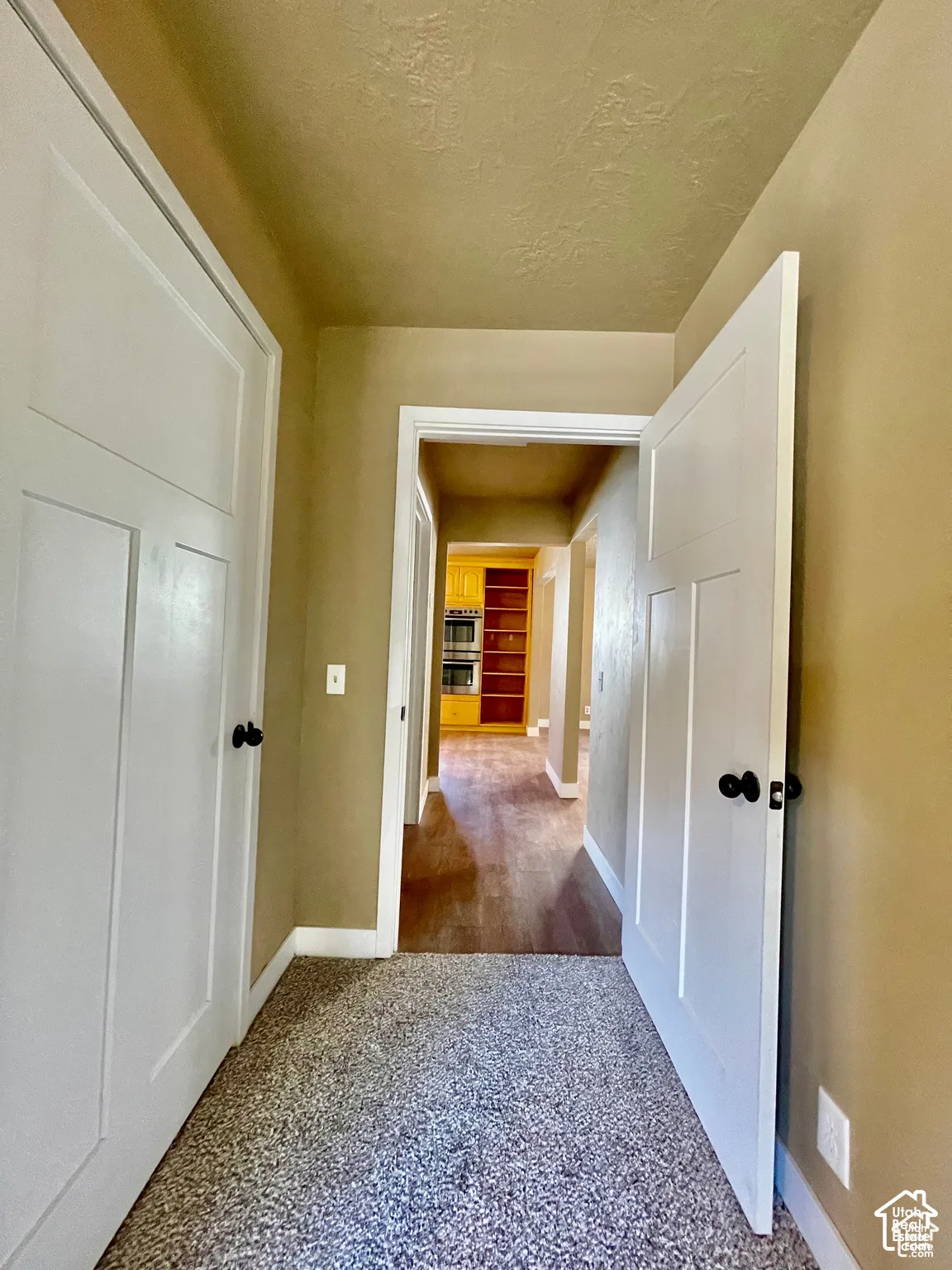 Hallway featuring two white panel doors with matte black hardware, textured tan walls, and carpet flooring