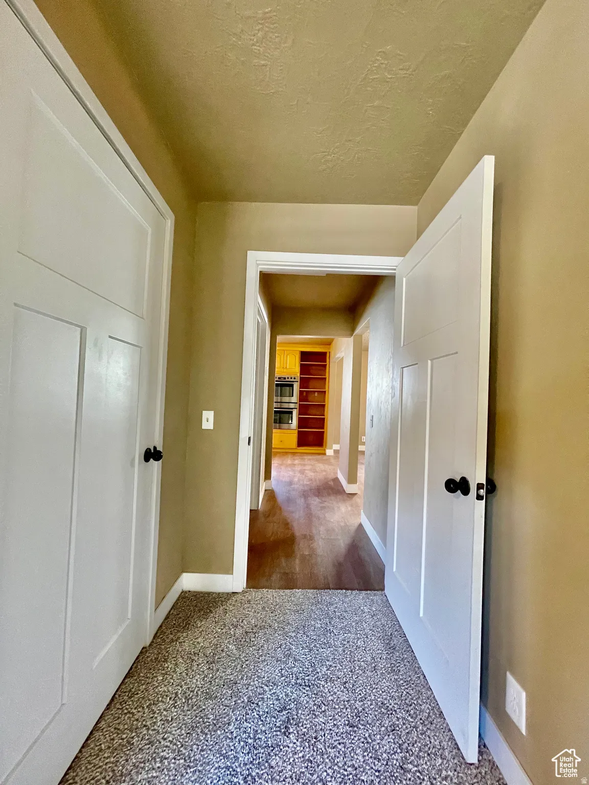 Hallway featuring two white panel doors with matte black hardware, textured tan walls, and carpet flooring