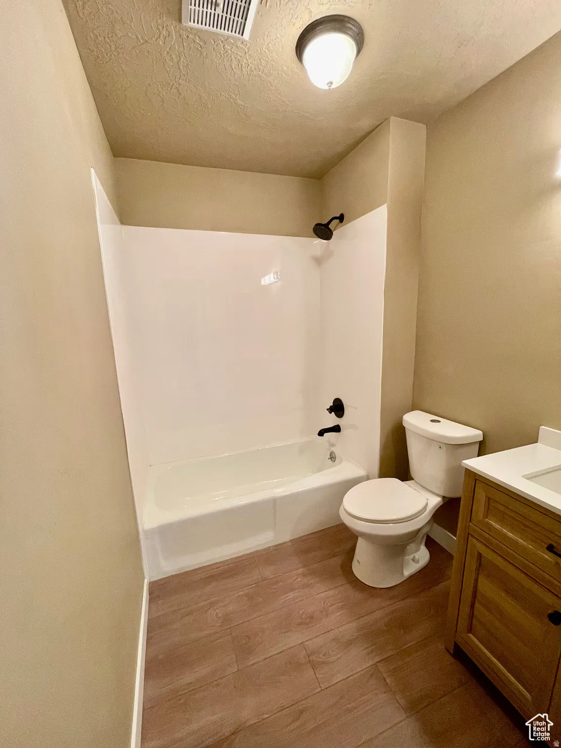 Bathroom featuring a white tub/shower combination with black fixtures, a white toilet, and a wood-finish vanity with a light-colored countertop