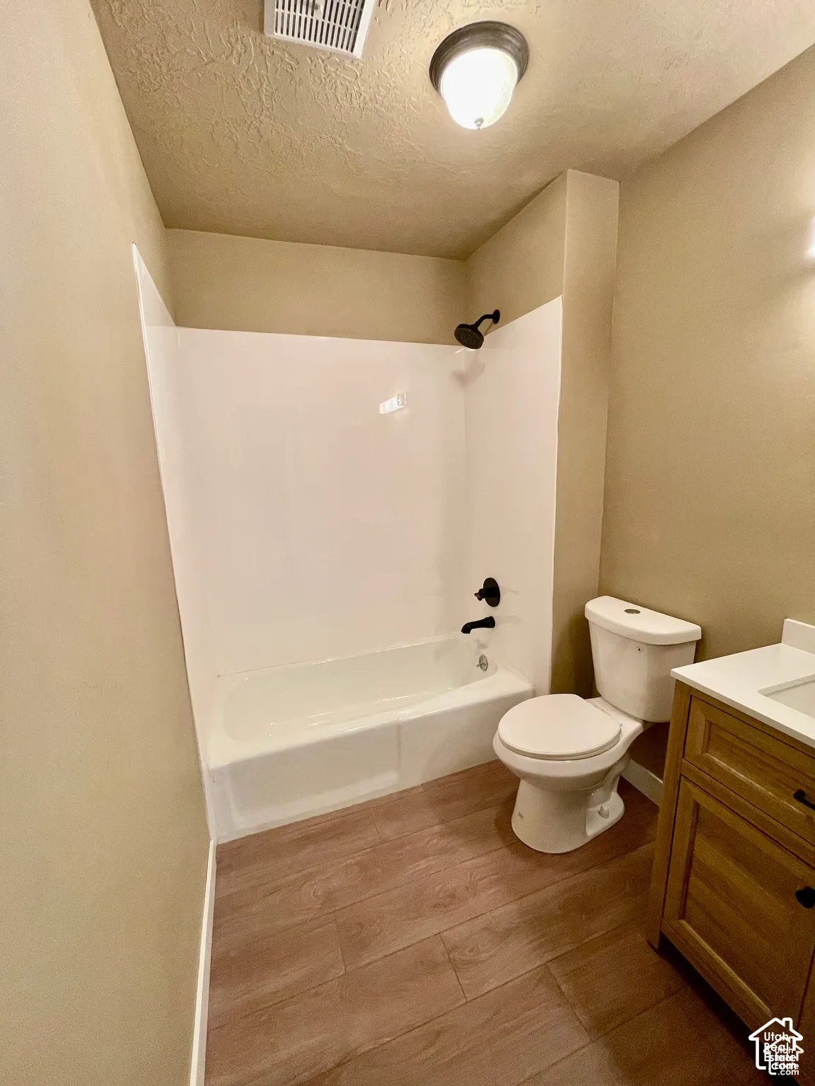 Bathroom featuring a white tub/shower combination with black fixtures, a white toilet, and a wood-finish vanity with a light-colored countertop