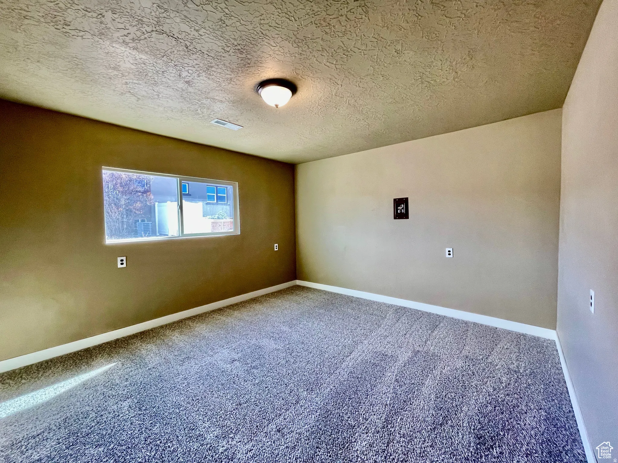 Carpeted room featuring a single window, a ceiling-mounted light fixture, neutral-toned walls, and white baseboards