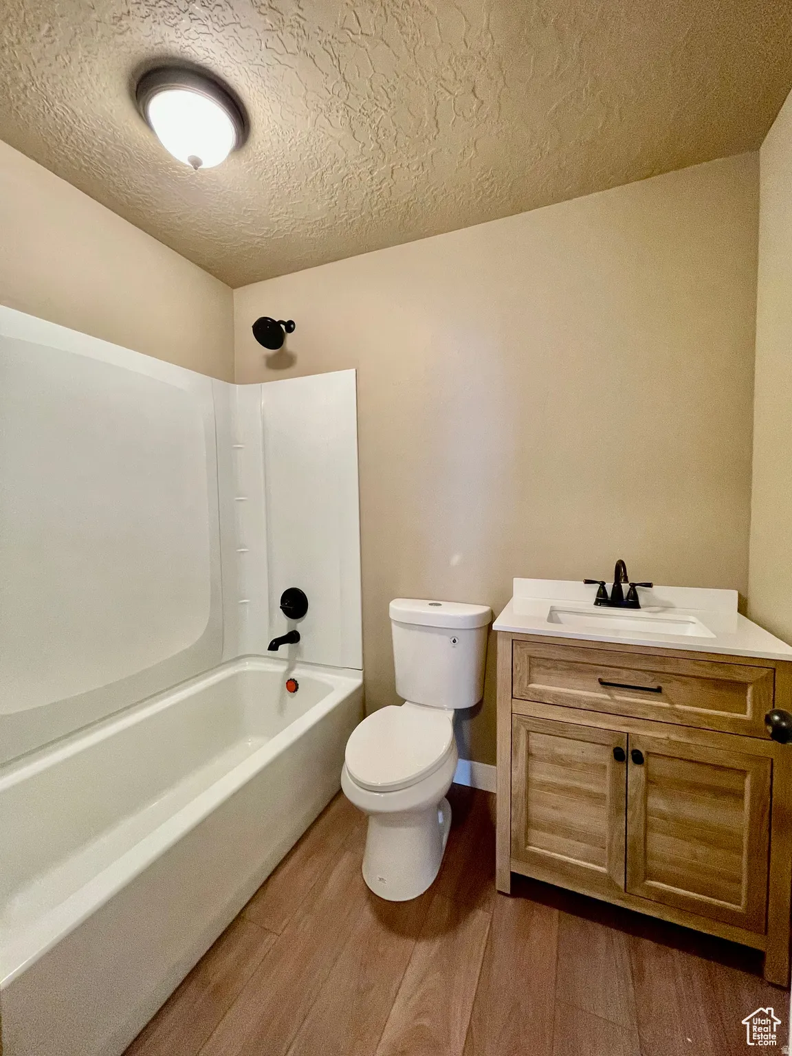 Bathroom featuring a white bathtub, toilet, and a wood-finish vanity with a white countertop and black fixtures