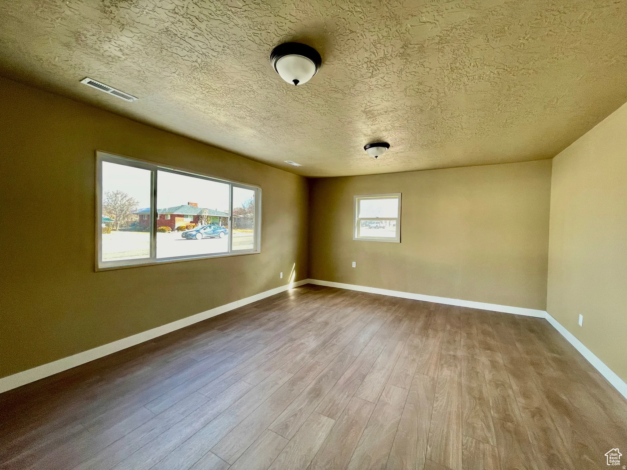 Expansive room featuring wood-finish flooring, two large windows, a smaller window, textured ceilings, and flush-mount lighting fixtures