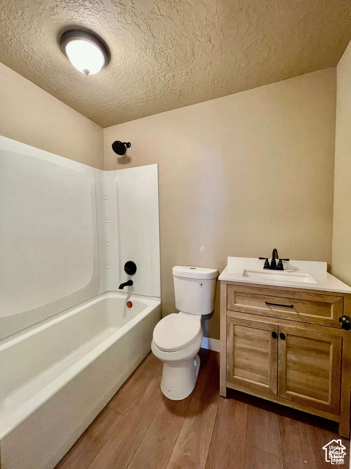 Bathroom featuring a white bathtub, toilet, and a wood-finish vanity with a white countertop and black fixtures