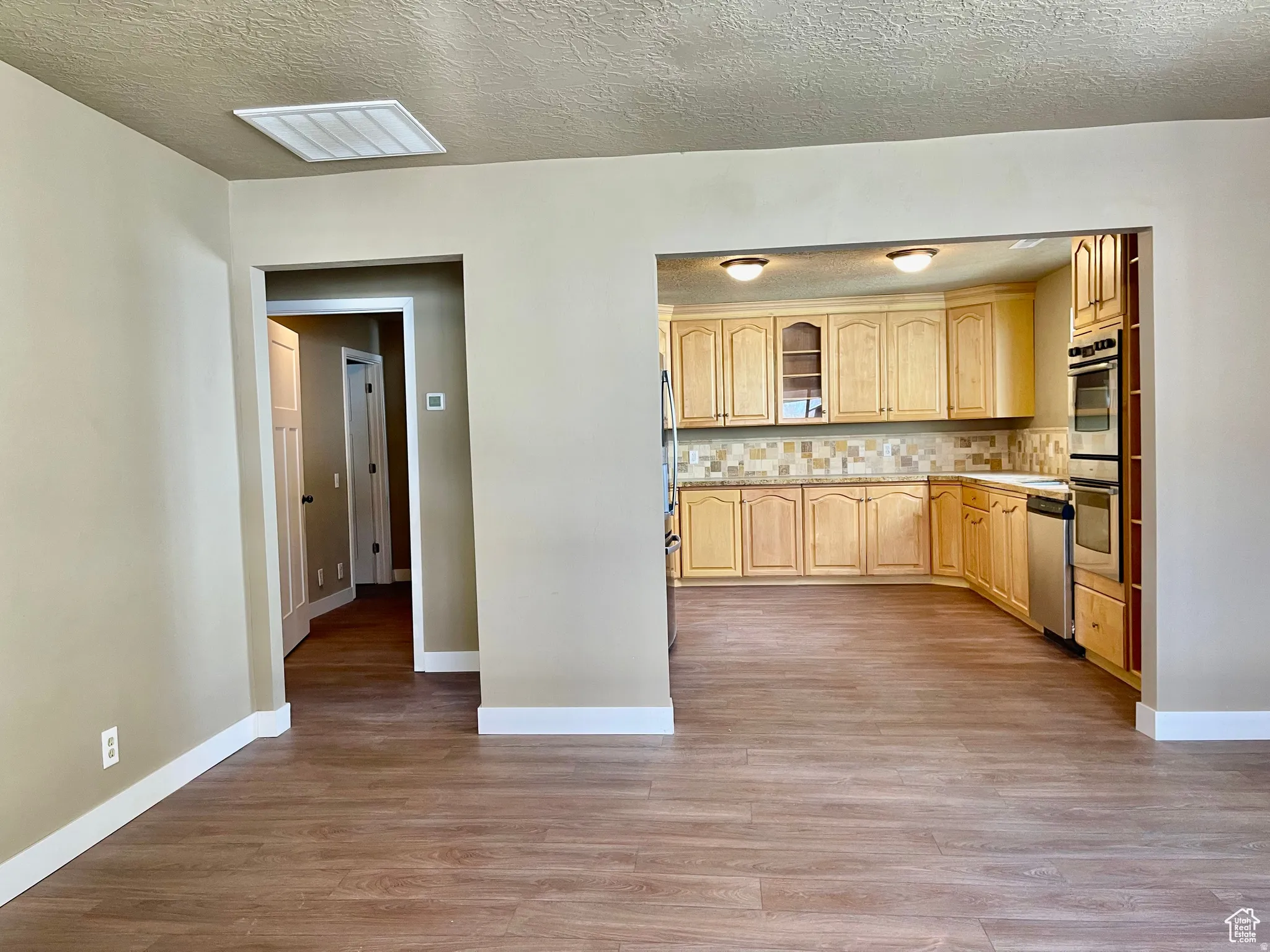 Kitchen featuring light wood cabinetry, a mosaic tile backsplash, stainless steel appliances, and ceiling-mounted lighting