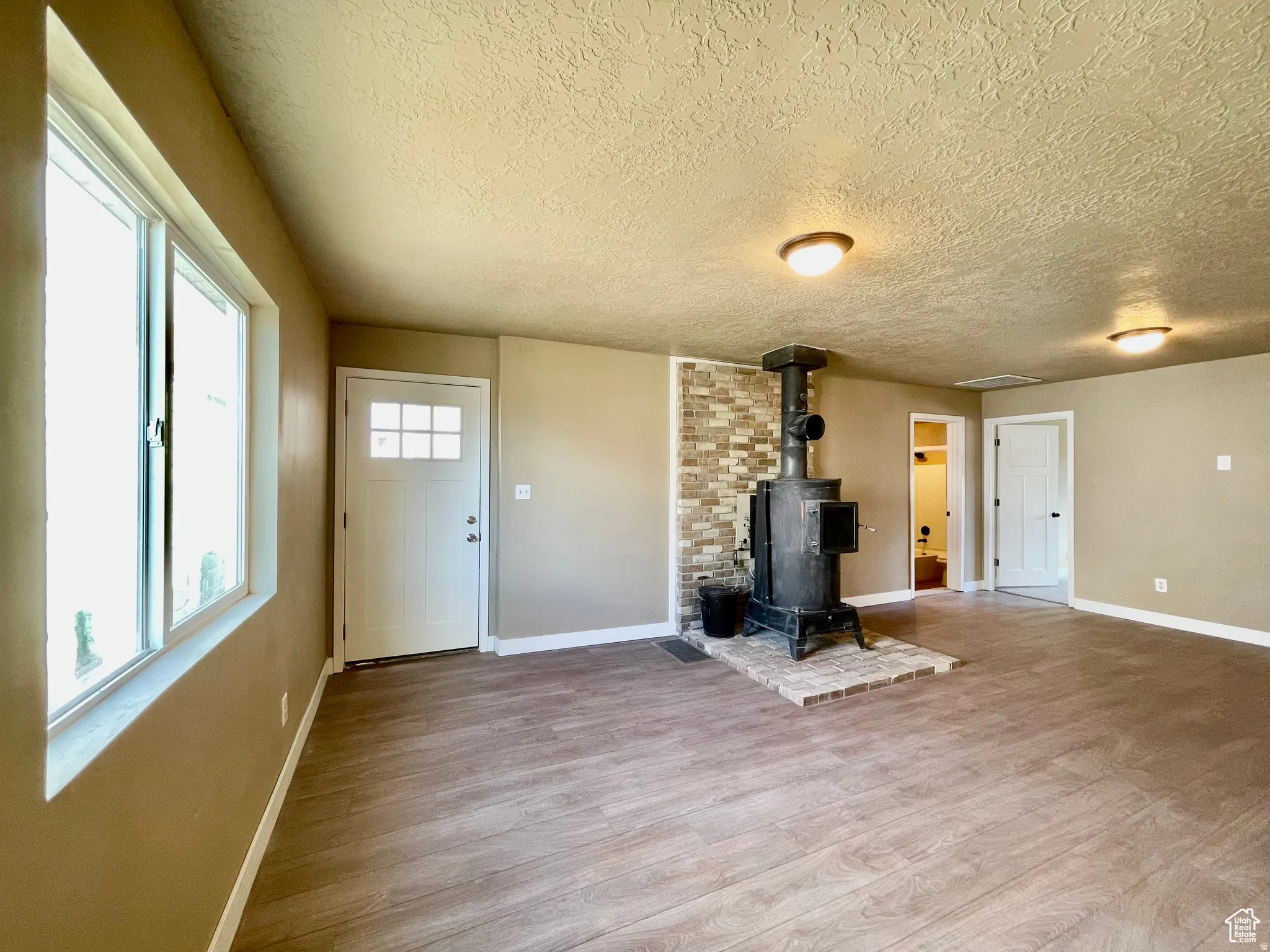 Spacious room featuring wood-finish flooring, a prominent wood-burning stove with a brick hearth, and a decorative stone accent wall