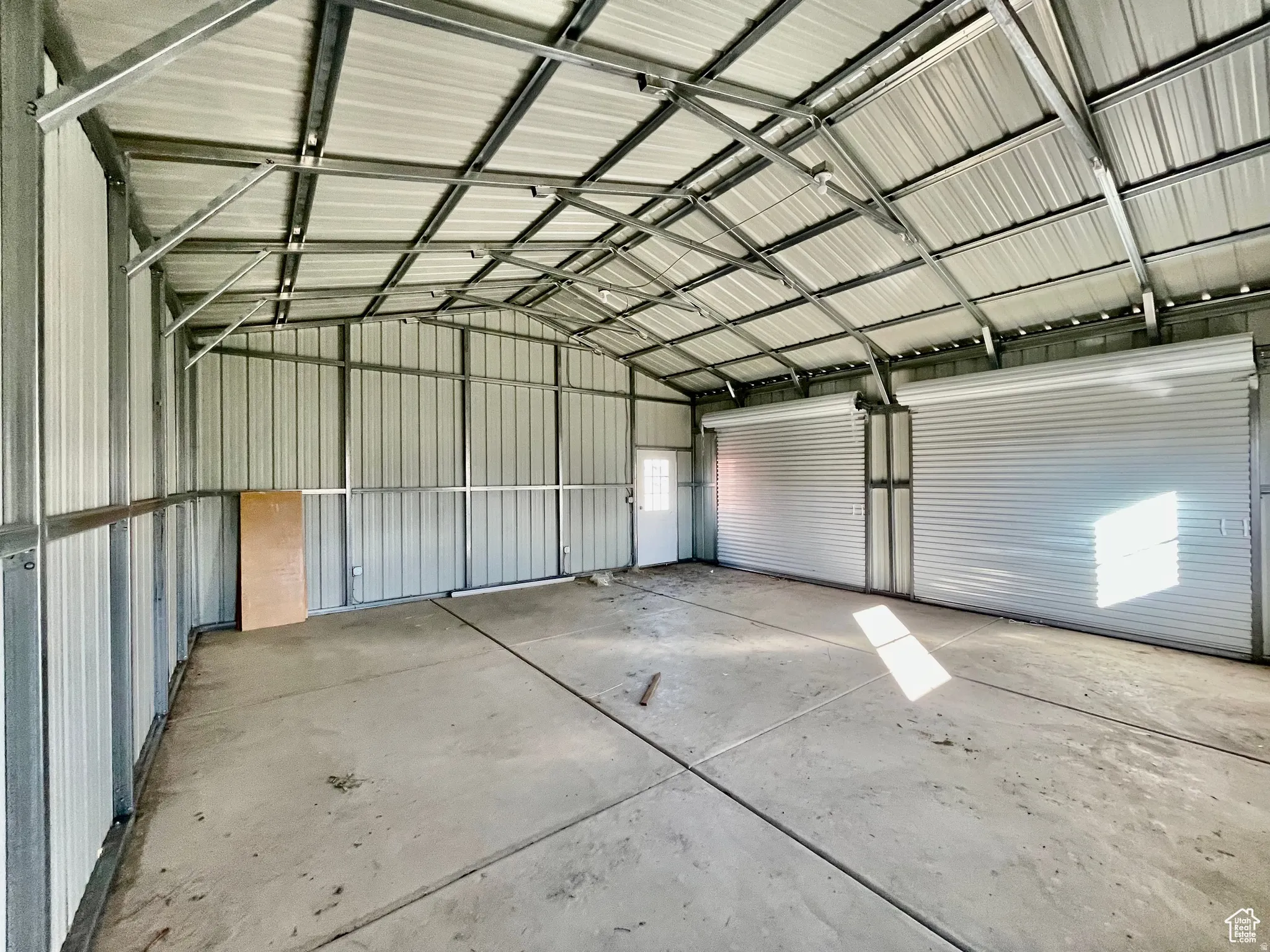 Spacious metal building with a concrete floor, two roll-up doors, a side entry door, and exposed metal truss ceiling