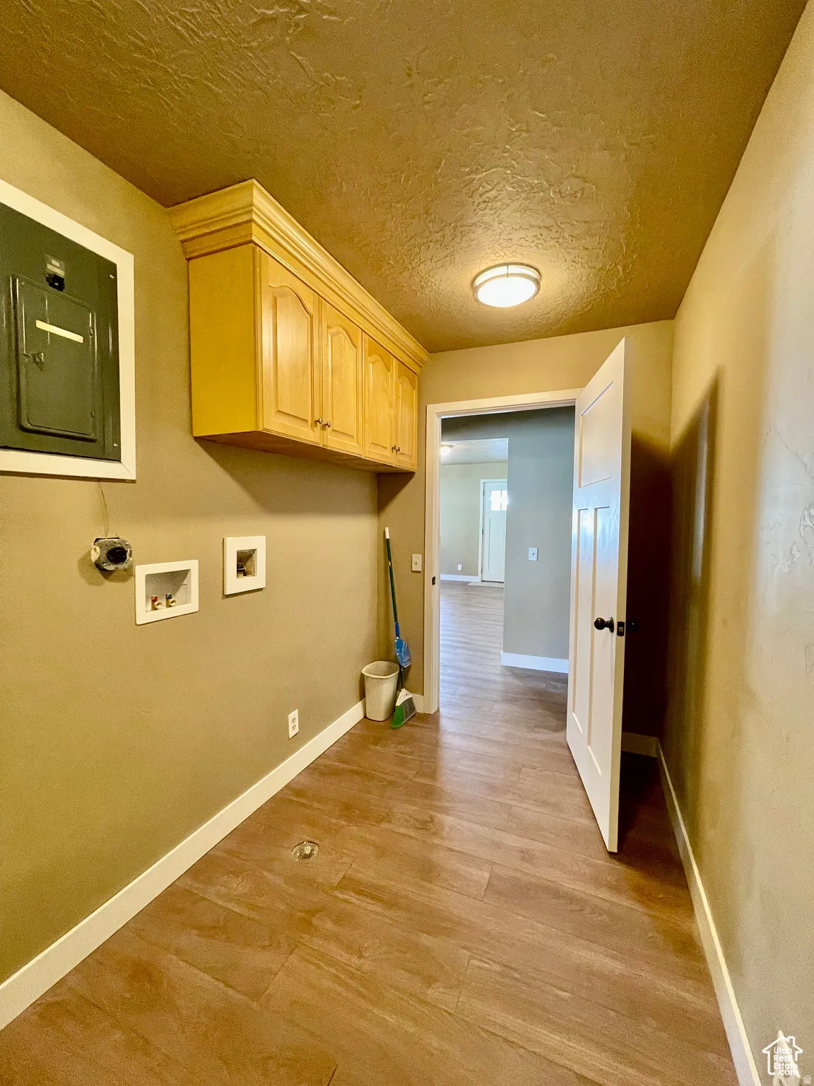 Dedicated utility area featuring wood-finish flooring, built-in cabinetry, overhead lighting, and white baseboards