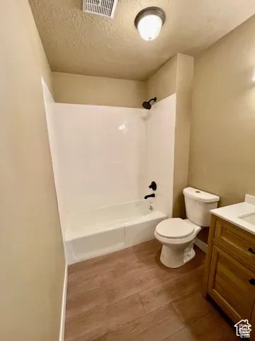 Bathroom featuring a white tub/shower combination with black fixtures, a white toilet, and a wood-finish vanity with a light-colored countertop