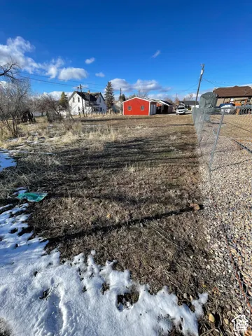 Expansive open lot featuring a red accessory building, partially visible chain-link fencing, gravel border, and a clear blue sky