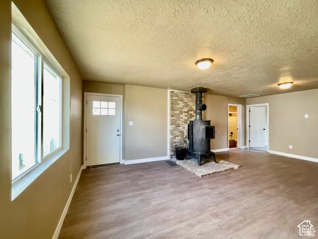 Spacious room featuring wood-finish flooring, a prominent wood-burning stove with a brick hearth, and a decorative stone accent wall