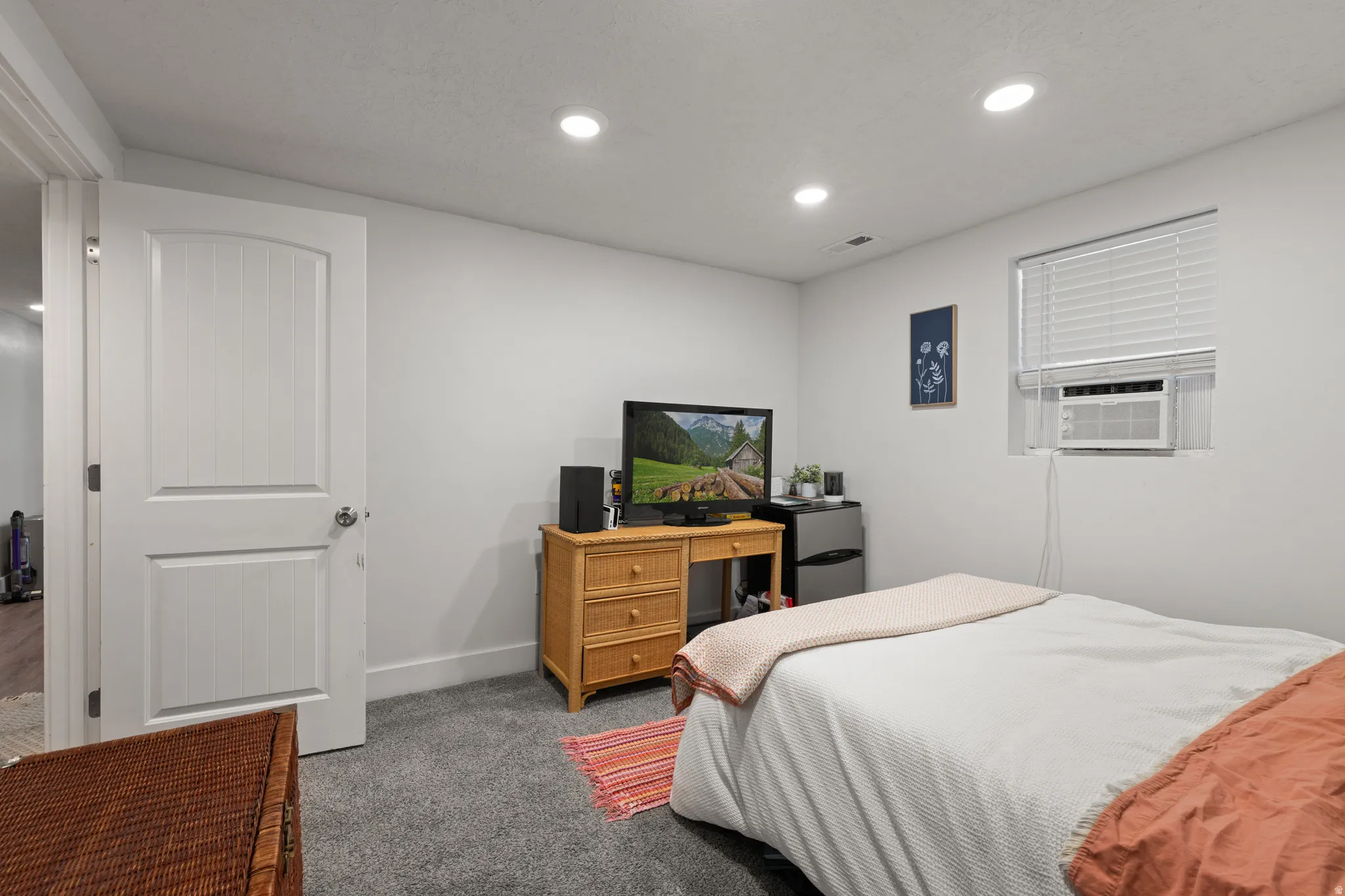 Recessed ceiling lighting illuminates a room featuring gray carpeting, white walls, and a white interior door with paneling