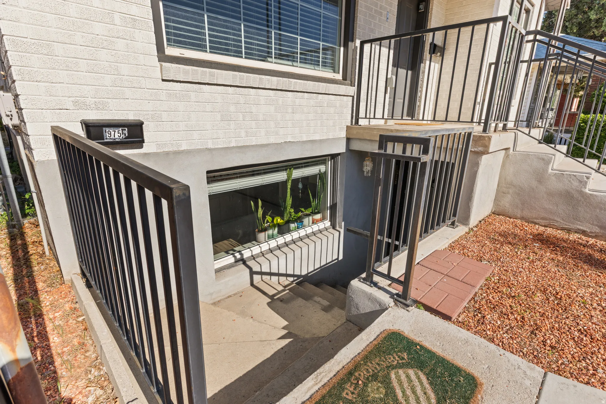 Exterior entry featuring concrete stairs, black metal railings, and a window well with a security grate