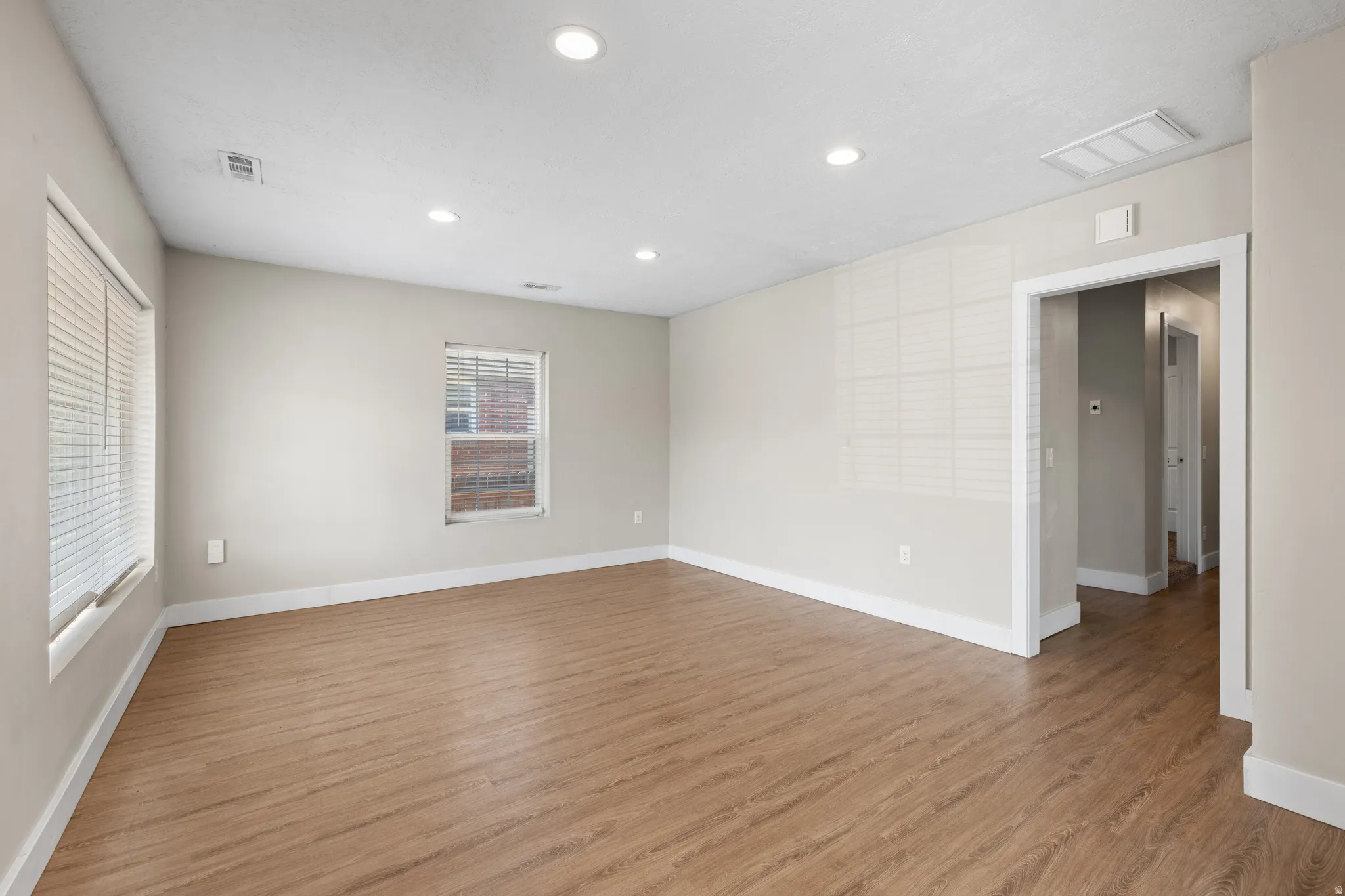 Spacious room featuring wood-finish flooring, recessed ceiling lighting, and multiple windows with blinds