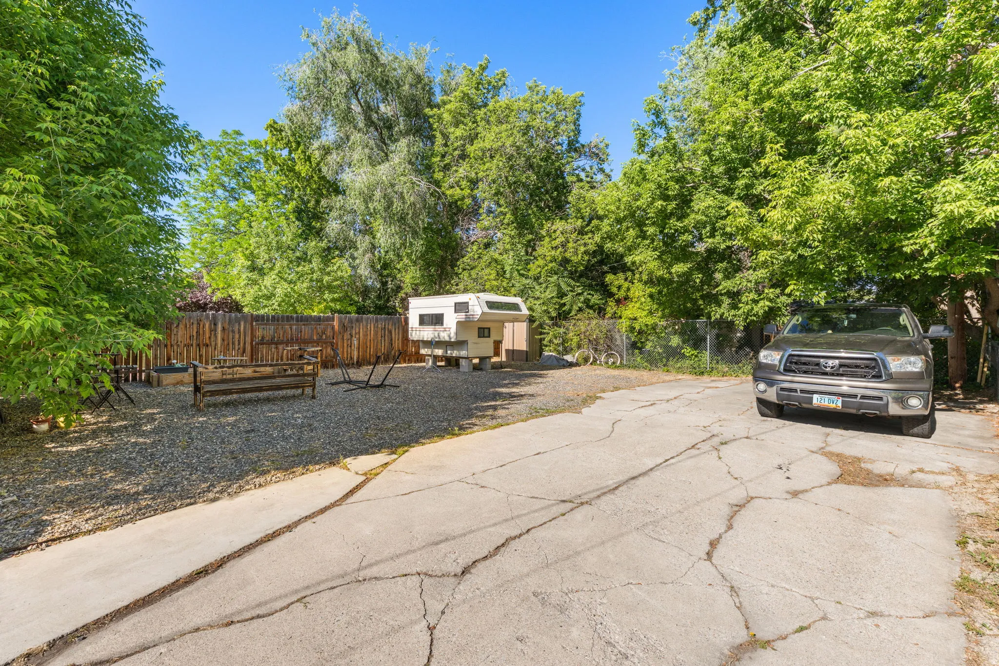 Spacious gravel yard area featuring a wood privacy fence and mature trees