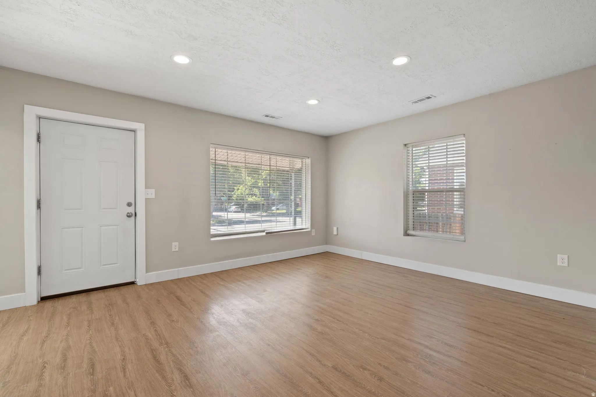 Spacious room featuring wood-finish flooring, recessed lighting, neutral wall tones, white trim, and multiple windows with blinds