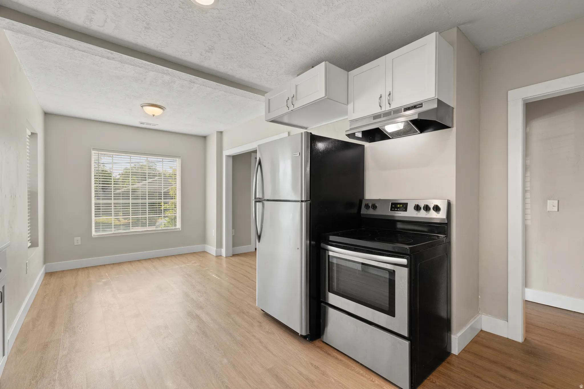 Kitchen area with stainless steel appliances, white cabinetry, and wood-finish flooring